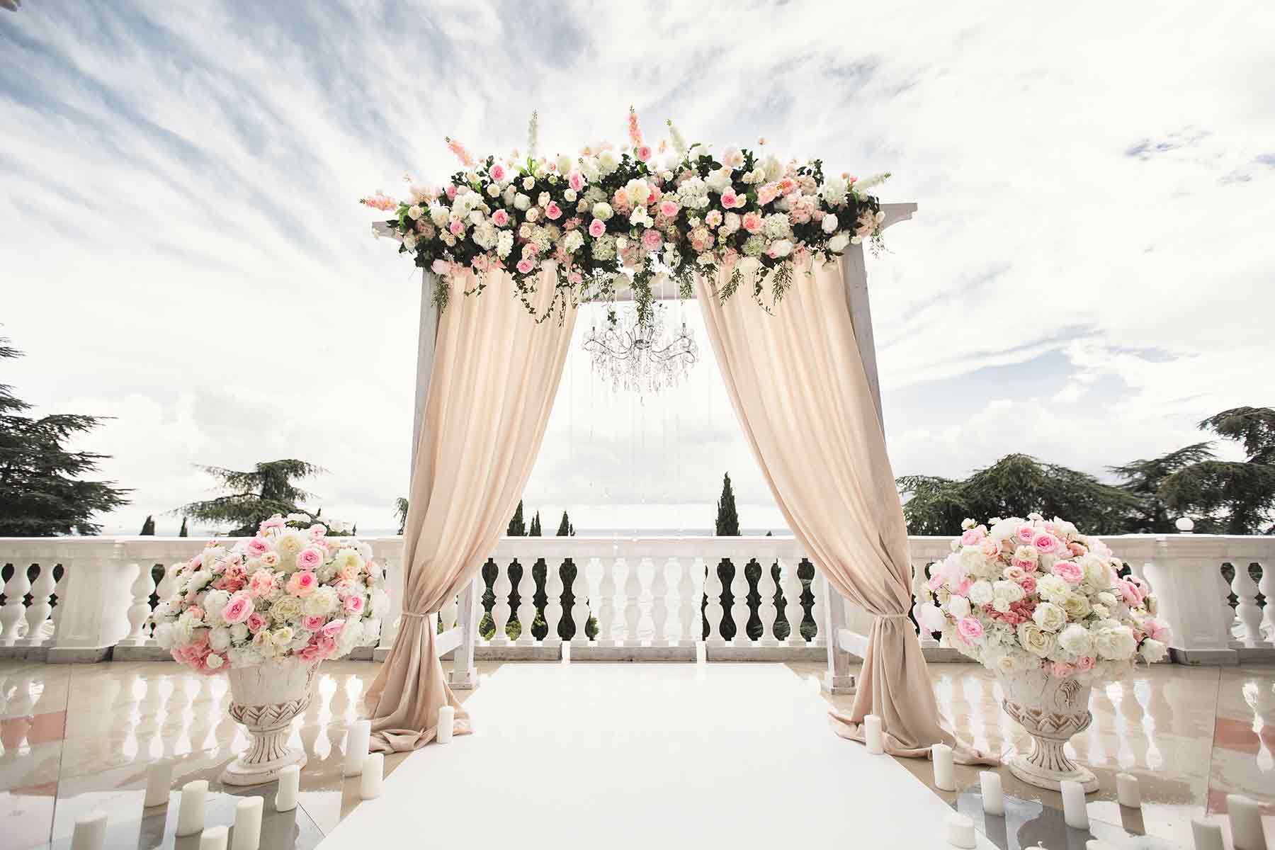 Elegant outdoor wedding arch decorated with flowers and draped curtains