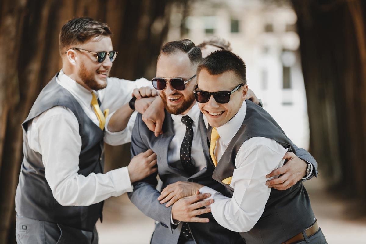 Groomsmen in black sunglasses and rental tux hug having fun at the wedding