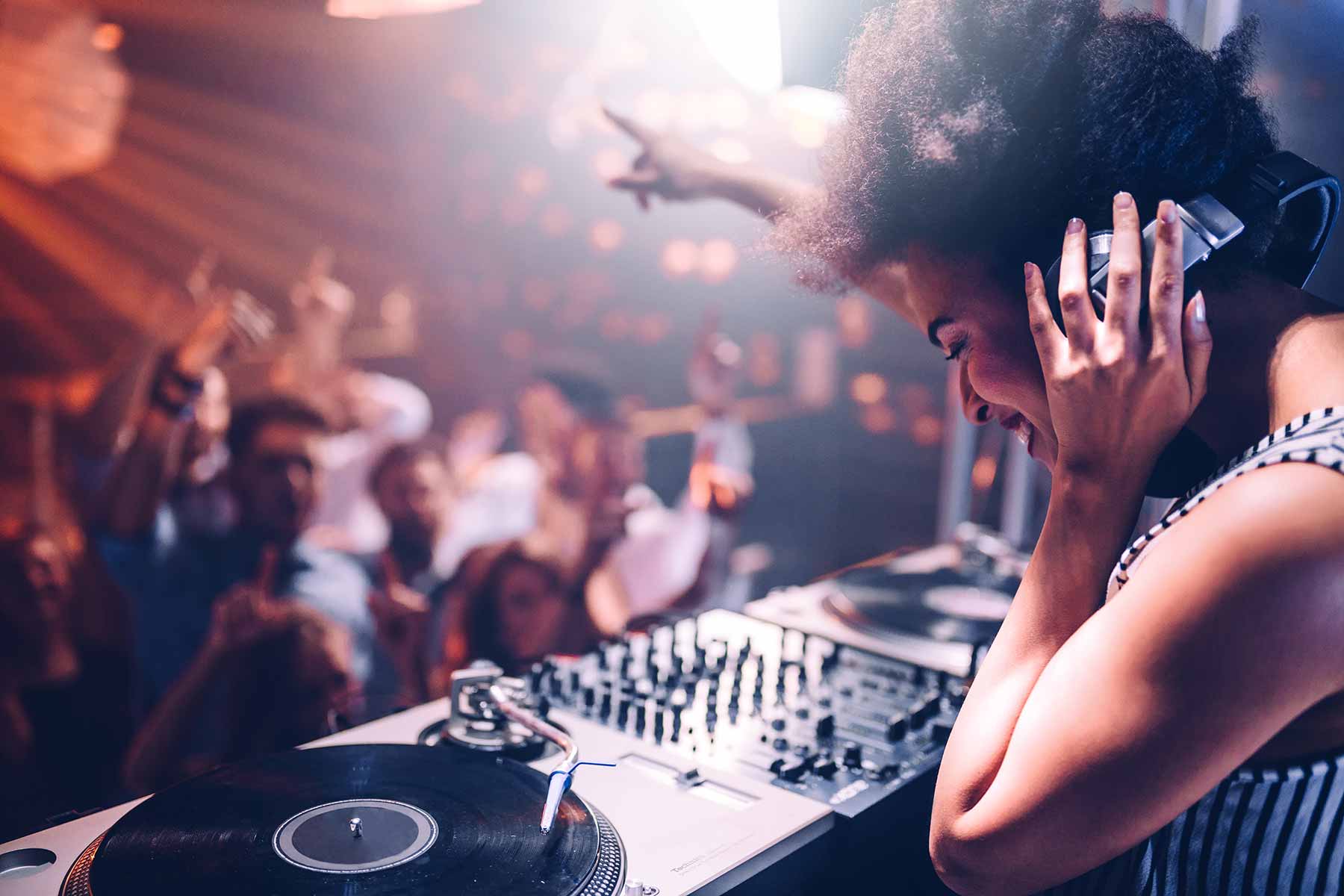 Young female DJ playing music at the club while the audience dances to the beat Young female DJ playing music at the club while the audience dances to the beat
