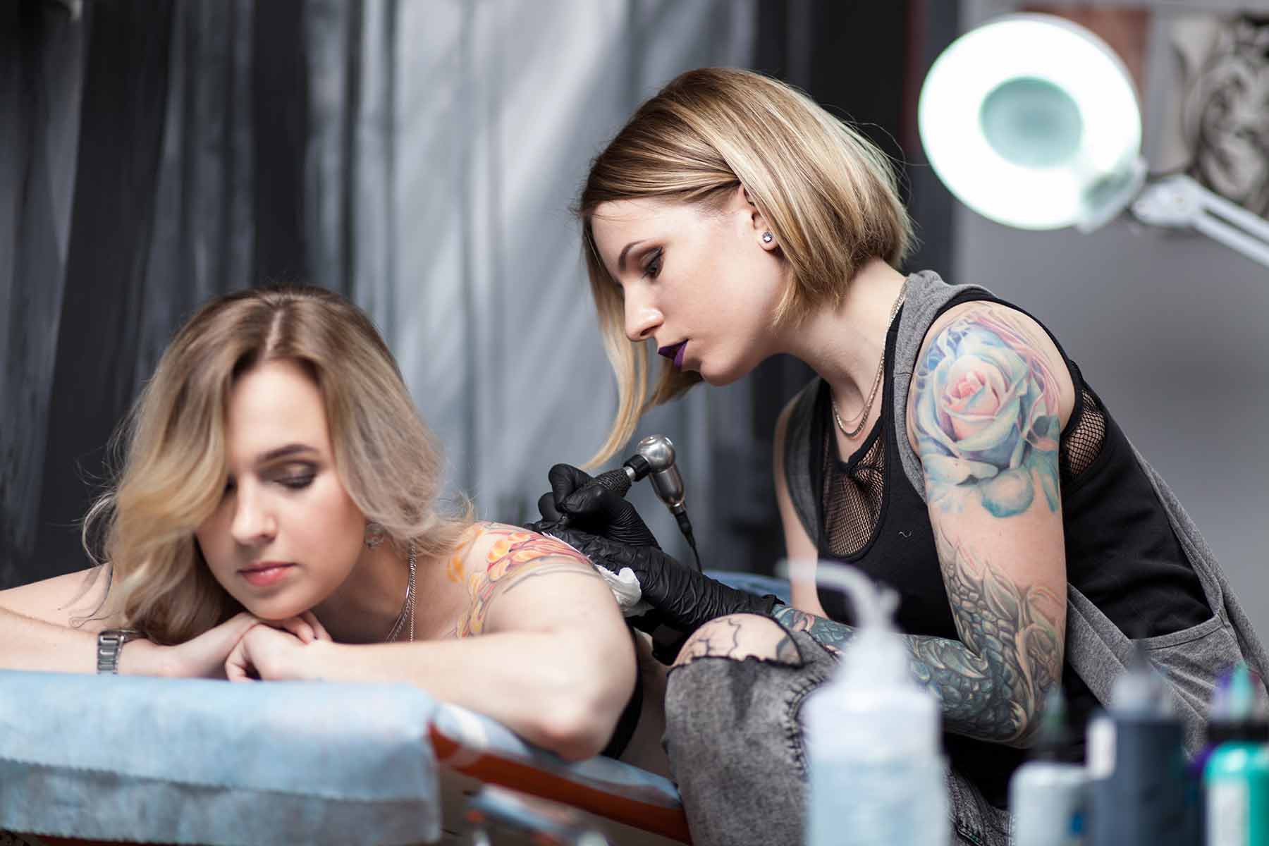 A female tattoo artist creating a colorful shoulder tattoo on client