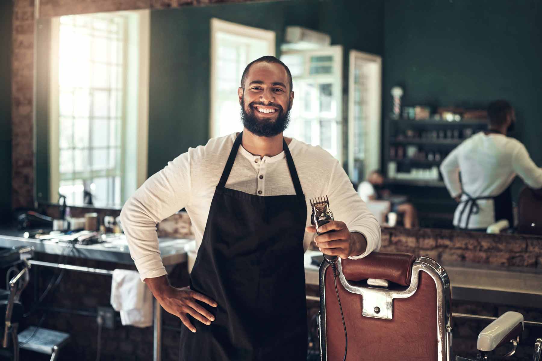 A barber with hair trimmer clippers standing next to a chair in a barbershop A barber with hair trimmer clippers standing next to a chair in a barbershop